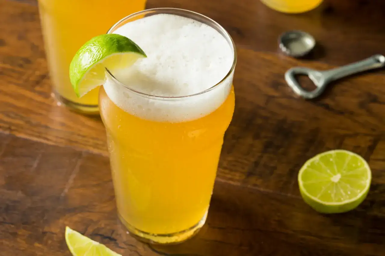 Orzeźwiający radler co to? To piwo z lemoniadą, podane z plasterkiem limonki, na drewnianym stole.